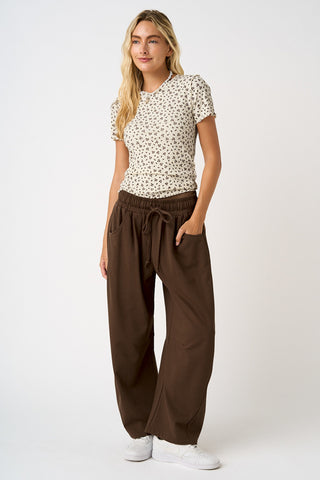 Woman wearing a patterned top and brown wide-leg pants on a white background