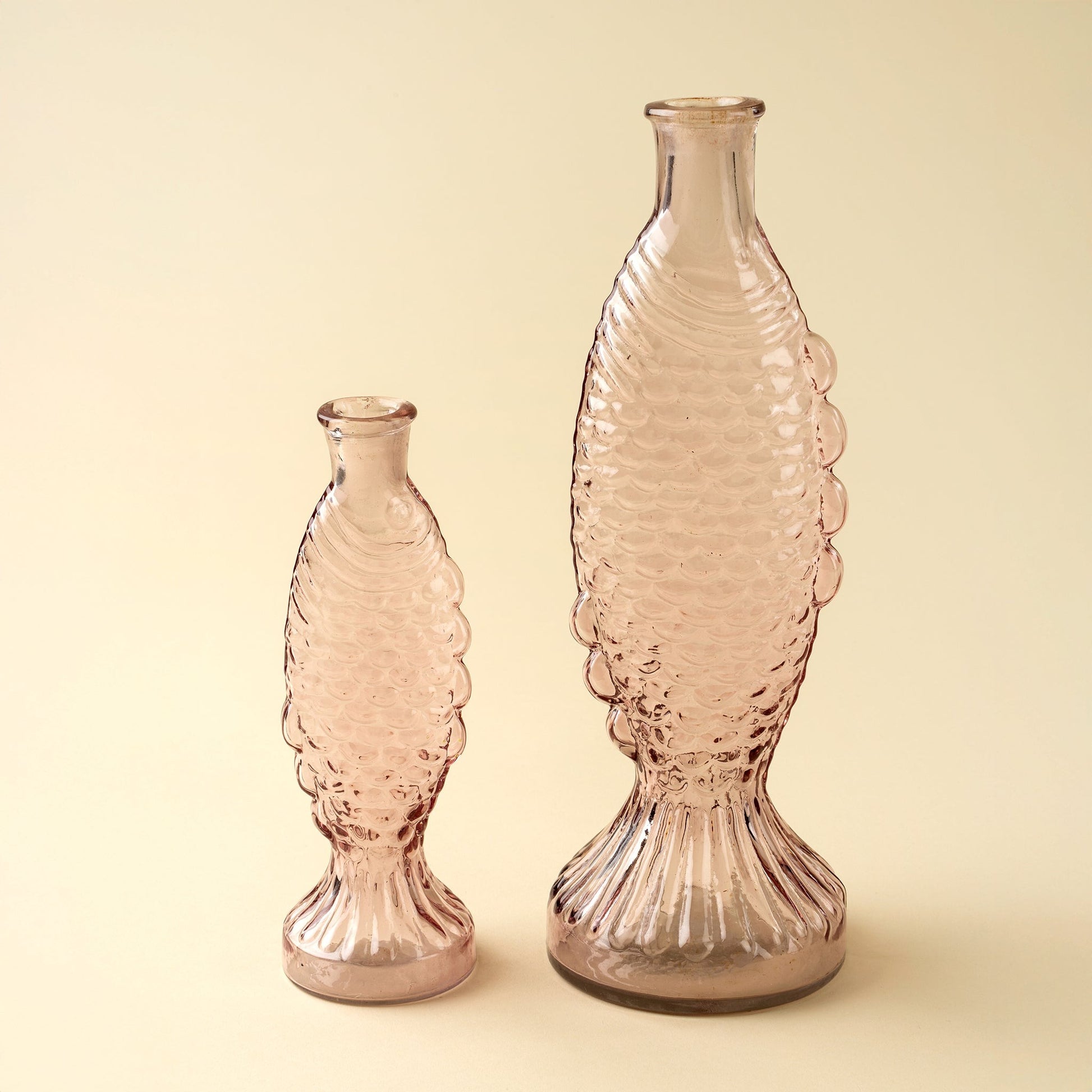Two pink fish glass vases with textured design on a beige background