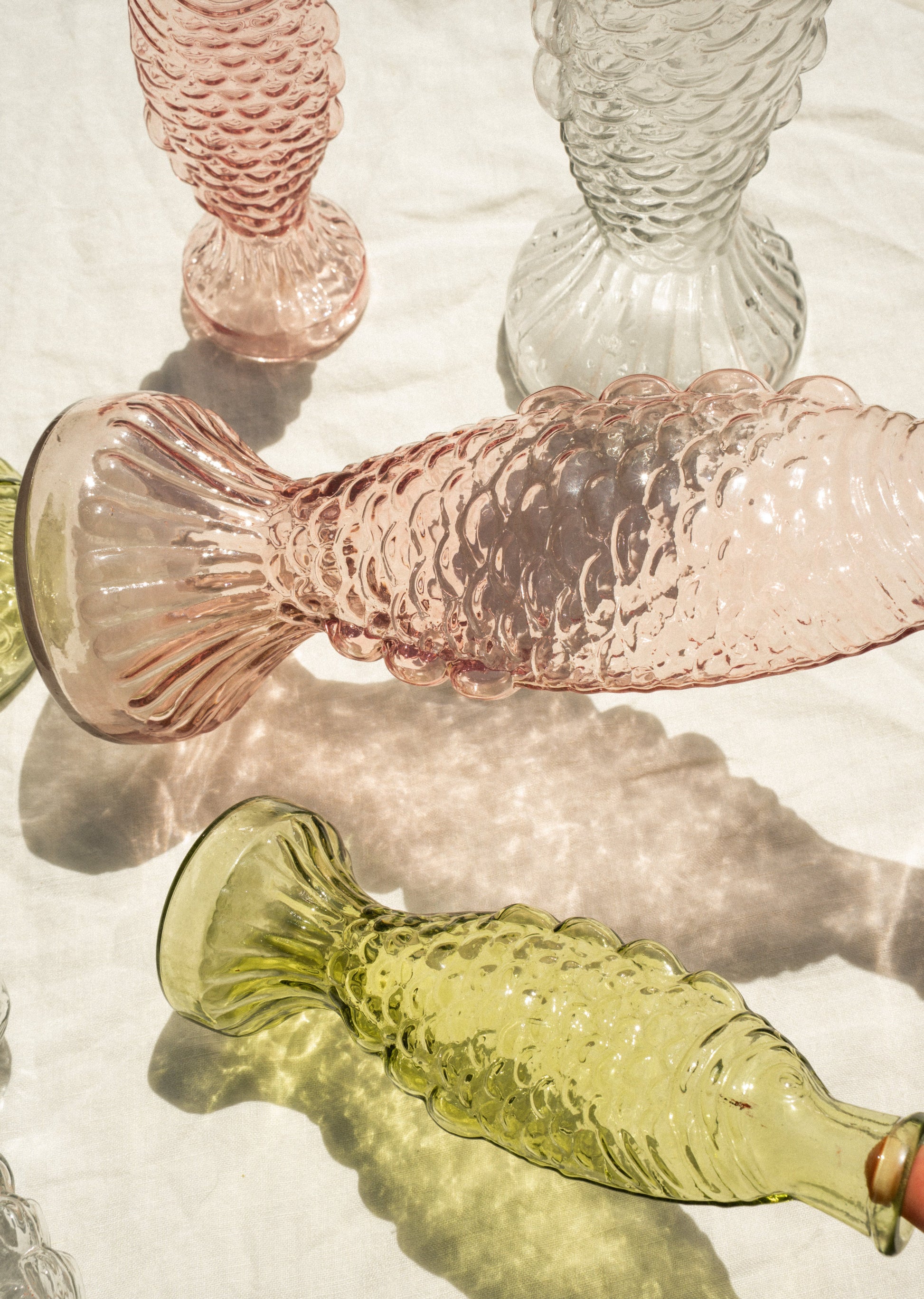 Glass fish-shaped objects in pink and green on a white surface