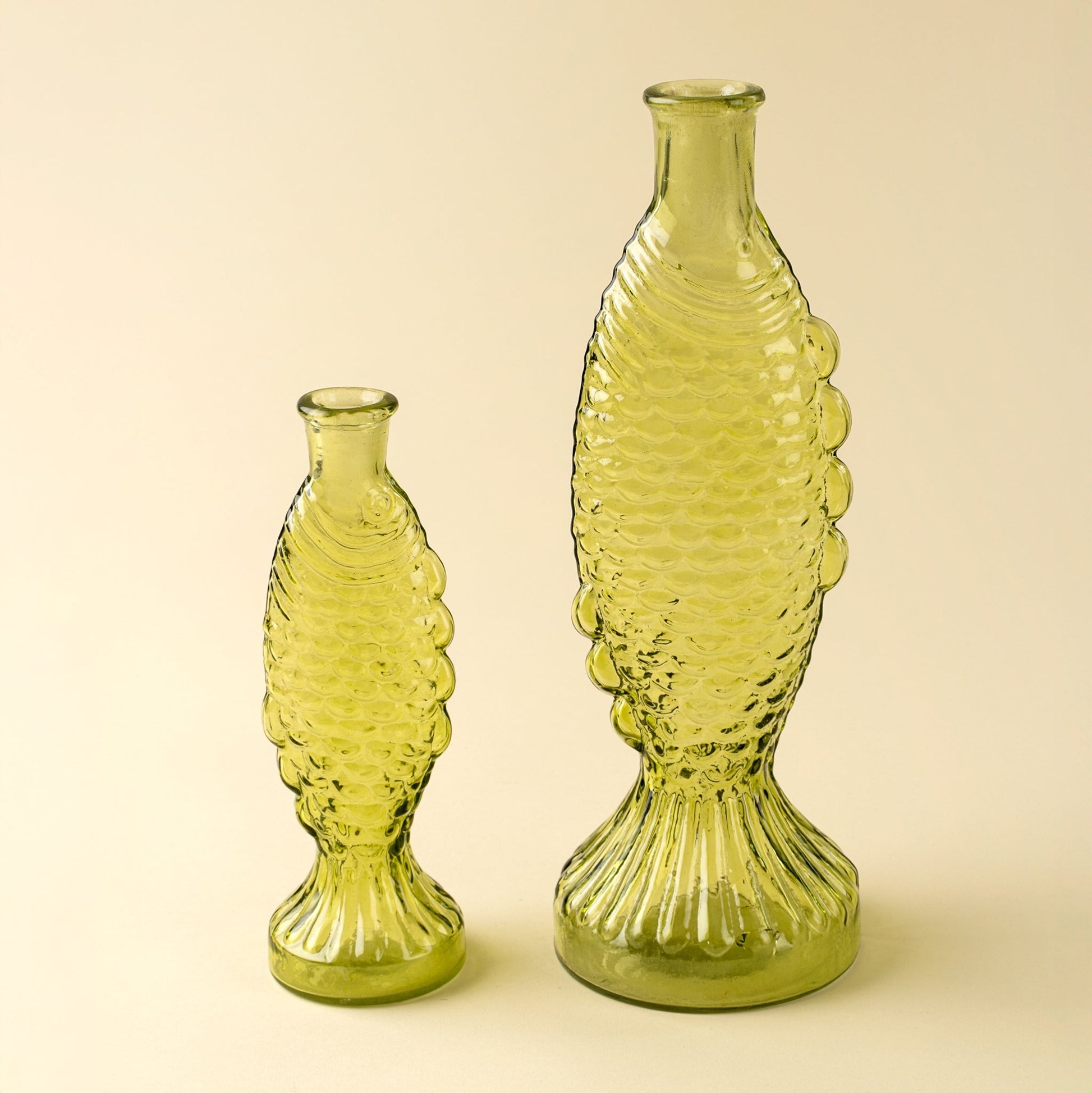 Two green fish glass vases with textured design on a beige background
