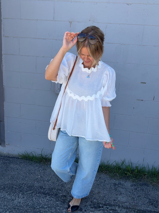 Woman wearing a white blouse and light blue jeans against a gray wall.