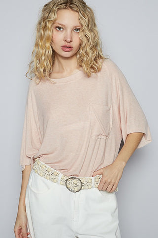 Woman wearing a light pink top and white pants with a decorative belt against a plain background