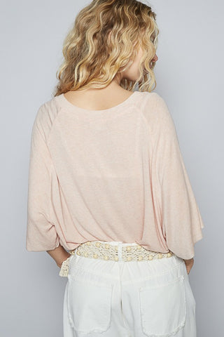 Woman wearing a light pink top and white pants with a decorative belt against a plain background