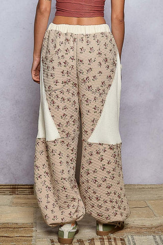 Person wearing beige floral pants with white accents on a plain background