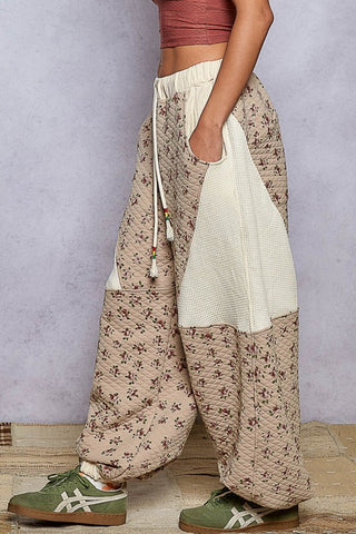 Person wearing floral wide-leg pants with a plain white top and green shoes on a gray background