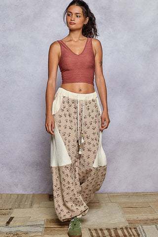 Woman wearing a rust-colored top and beige floral pants against a gray background