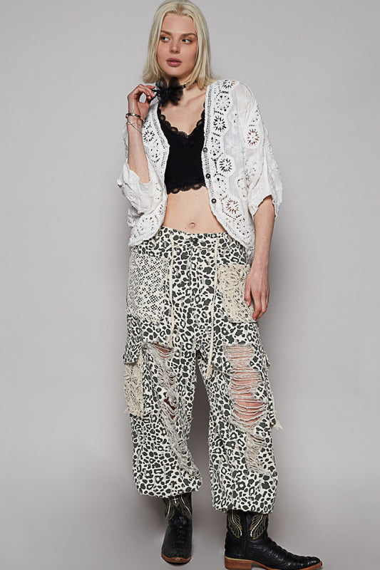 Woman wearing a white lace jacket and leopard print pants against a gray background