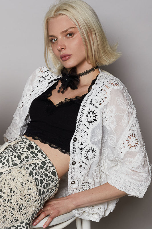Woman wearing a white lace cardigan over a black top and leopard print pants on a gray background