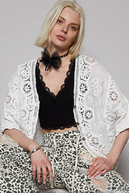 Woman wearing a white lace cardigan over a black top and leopard print pants on a gray background