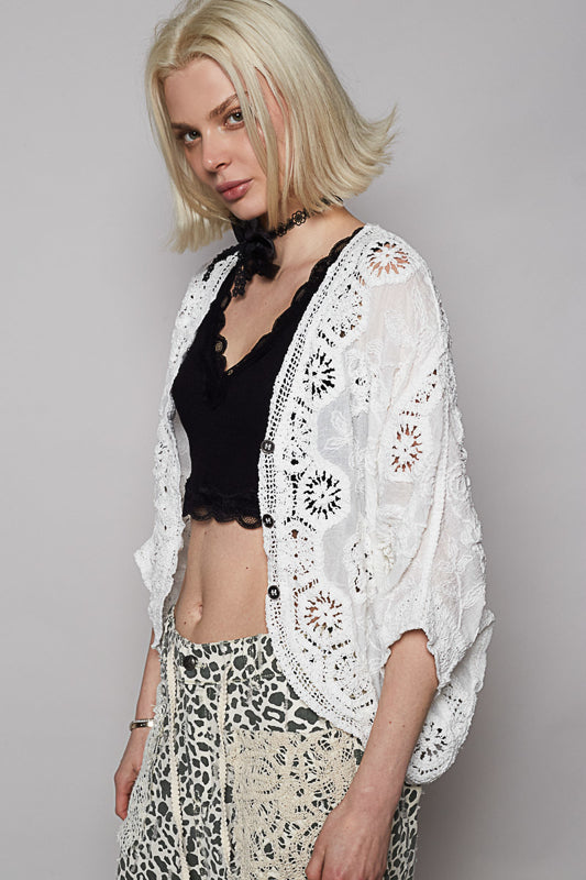 Woman wearing a white lace cardigan over a black top and leopard print pants on a gray background