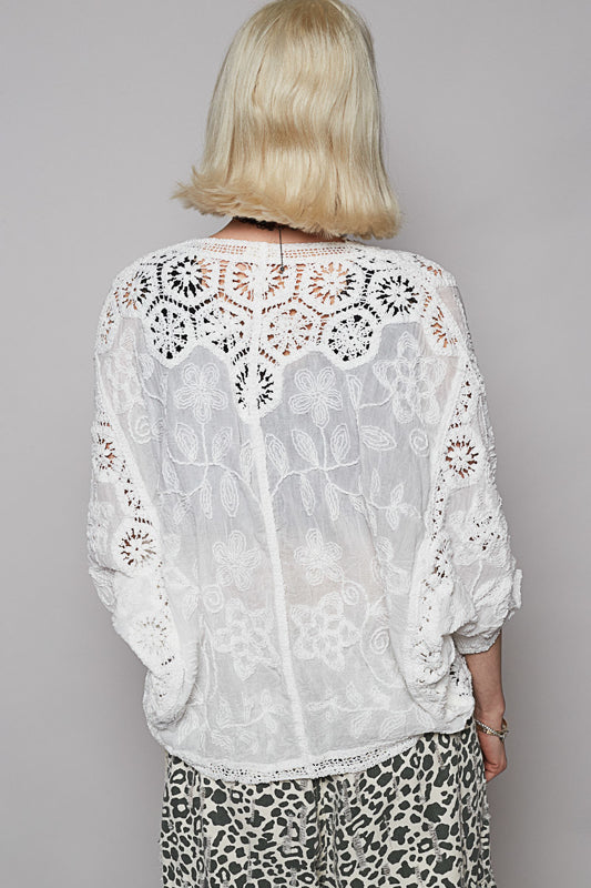 Person wearing a white lace blouse with a gray background