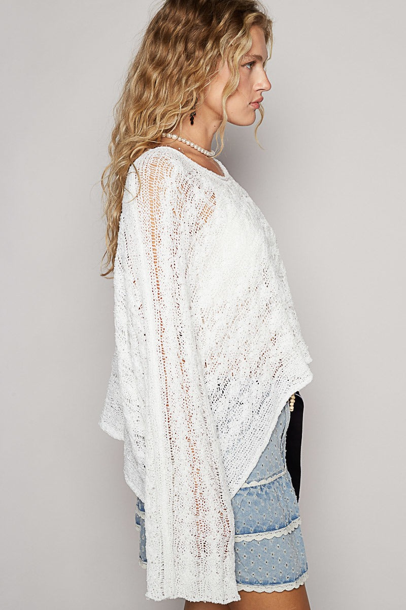 Woman wearing a white lace cover-up and denim shorts on a plain background