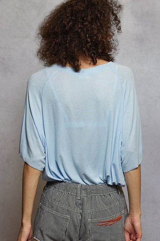 Person wearing a light blue top and gray pants against a gray background
