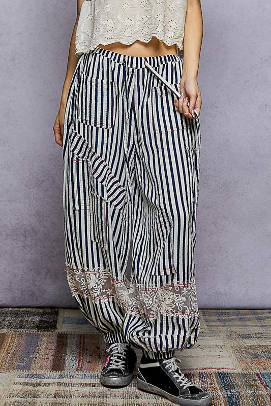 Person wearing black and white striped pants with floral patterns on a textured floor.