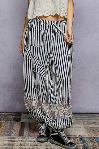 Person wearing black and white striped pants with floral patterns on a textured floor.