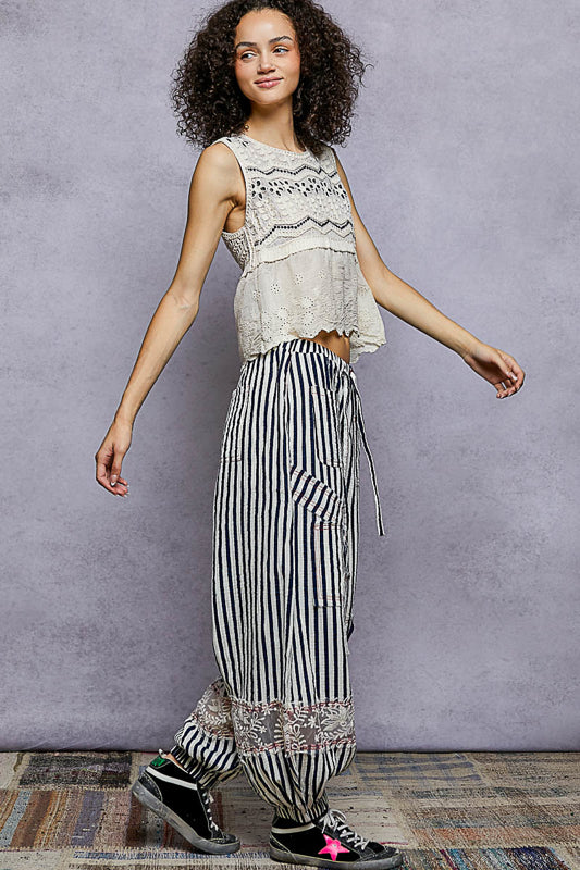 Woman wearing a sleeveless top and striped pants against a gray background