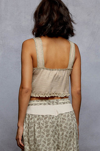 Woman wearing a beige sleeveless top and patterned pants against a gray background