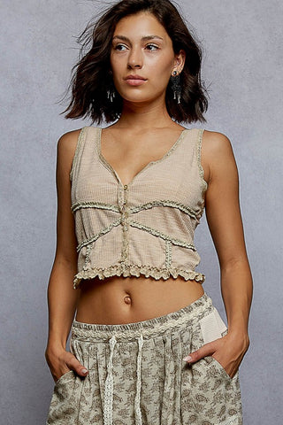 Woman wearing a beige lace top and patterned pants against a gray background