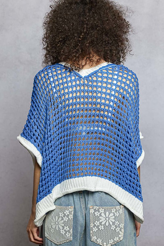 Person wearing a blue and white crocheted poncho against a gray background