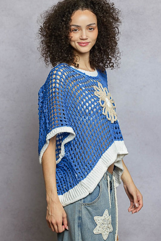 Woman wearing a blue and white crocheted poncho with starfish designs against a gray background
