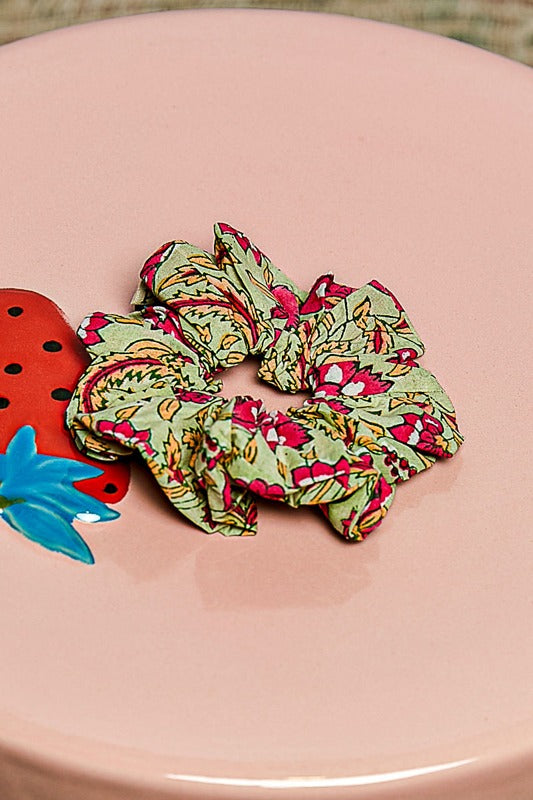 Two floral-patterned scrunchies on a pink surface with a strawberry-shaped object.