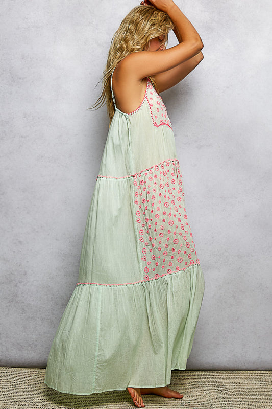 Woman wearing a light green dress with pink floral embroidery against a gray background