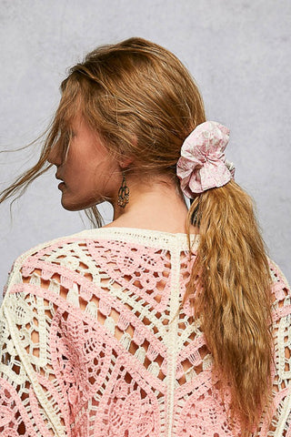 Woman with a pink scrunchie in her hair wearing a pink crochet cardigan.