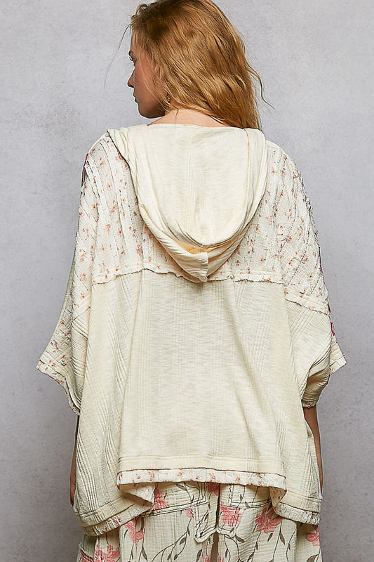 Woman wearing a light-colored, layered outfit with floral patterns against a plain background