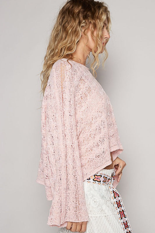 Woman wearing a pink lace kimono over a white outfit with floral patterns on a plain background