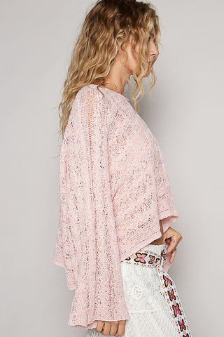 Woman wearing a pink lace kimono over a white outfit with floral patterns on a plain background