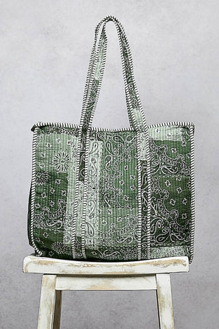 Green patterned tote bag on a wooden stool against a gray background