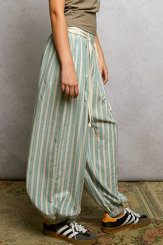 Person wearing striped pants and sneakers on a textured floor with a plain wall background