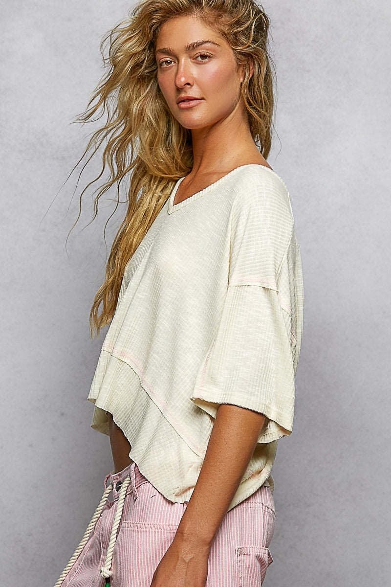 Woman wearing a light-colored top and pink pants against a gray background