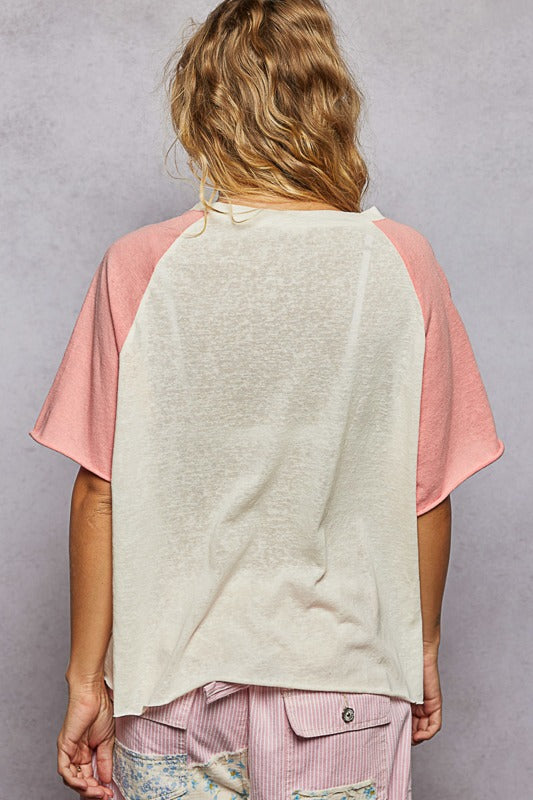 Person wearing a light-colored shirt with pink sleeves and pants against a gray background