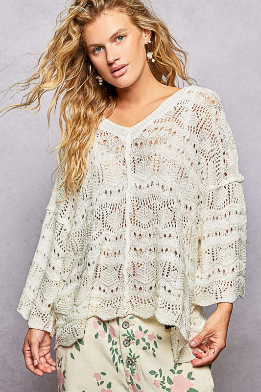 Woman wearing a white crochet top with floral pants against a gray background