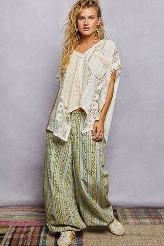 Woman wearing a white top and patterned pants against a plain background