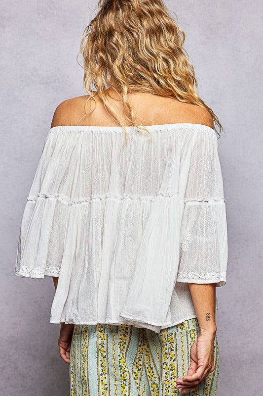 Woman wearing a white off-shoulder top with ruffled sleeves against a gray background