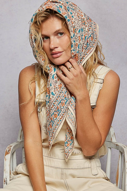 Woman wearing a patterned headscarf sitting on a chair against a plain background