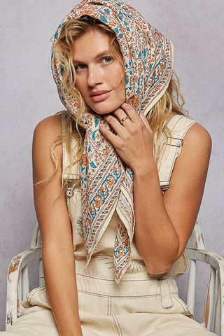 Woman wearing a patterned headscarf sitting on a chair against a plain background