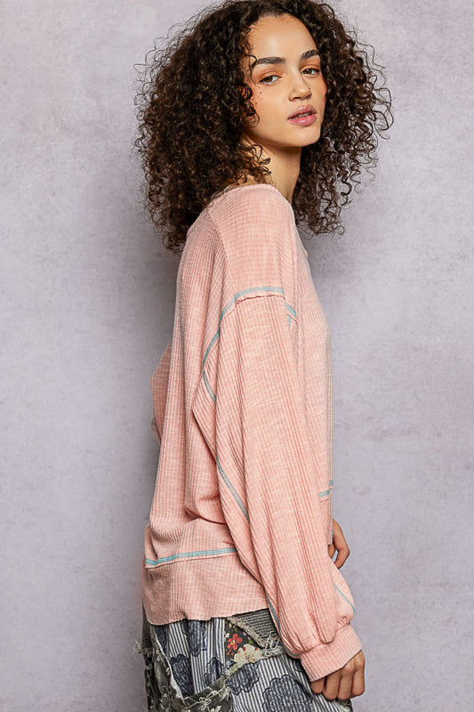 Women wearing a pink waffle knit top with blue seams on a grey background
