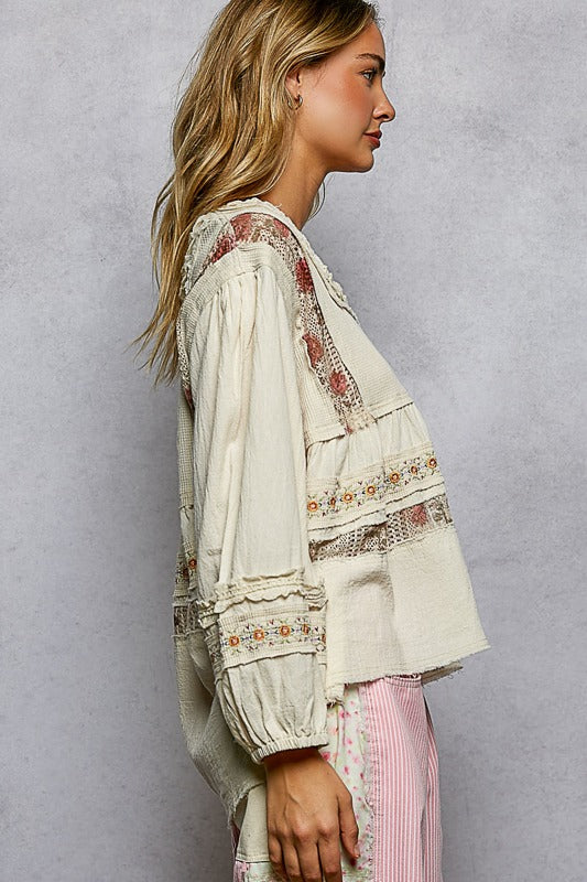 Woman wearing a white blouse with floral embroidery against a gray background
