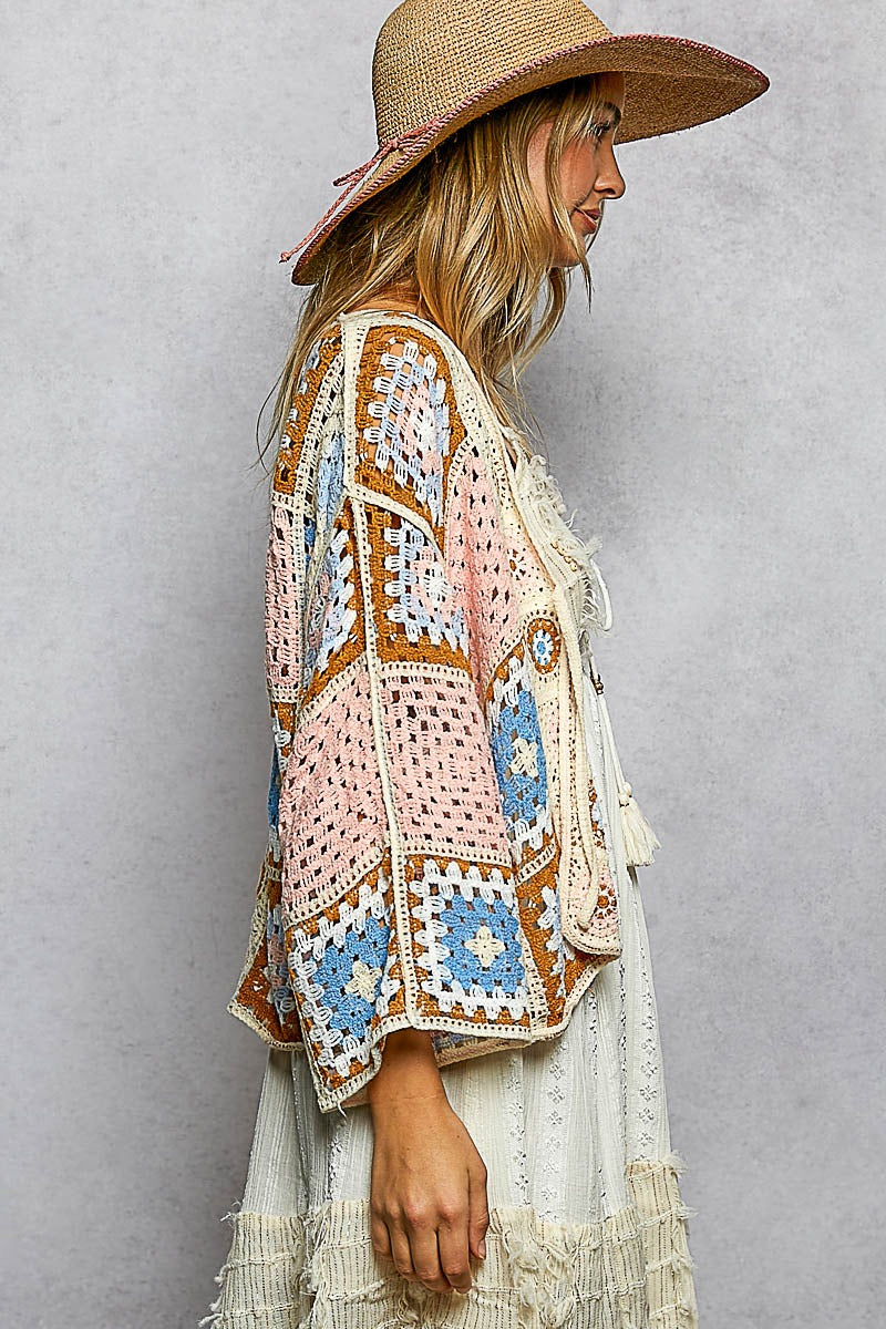 Woman wearing a colorful crochet cardigan and straw hat against a gray background