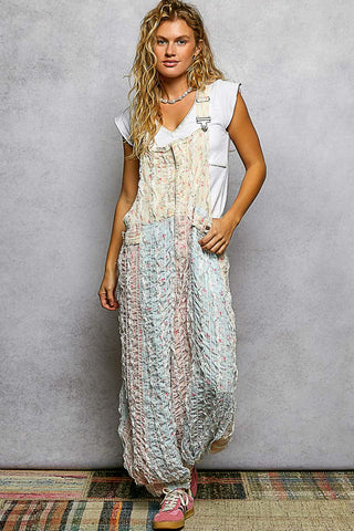 Woman wearing a long, patterned overall over a white shirt against a gray background