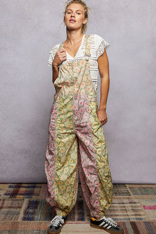 A women wearing floral printed overalls and a white top against a neutral background.