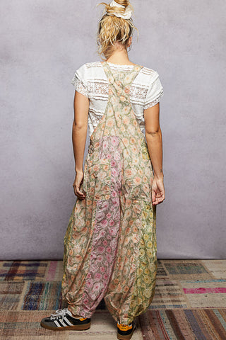 A women wearing floral printed overalls and a white top against a neutral background.