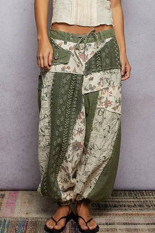 Person wearing a patchwork skirt with floral and geometric patterns on a plain background