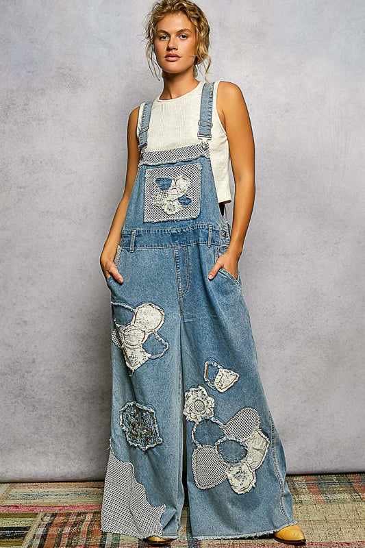 Woman wearing denim overalls with floral patches against a plain background