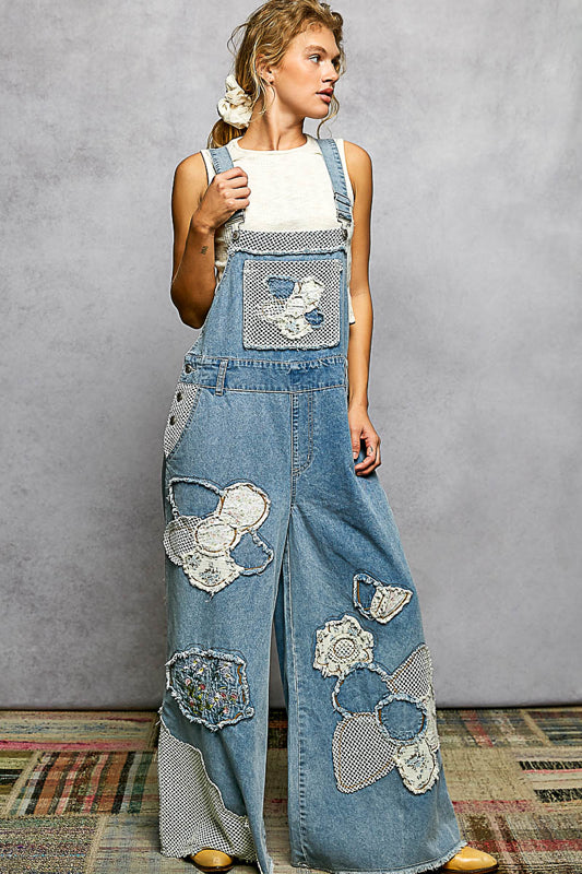Woman wearing denim overalls with floral patches against a gray background