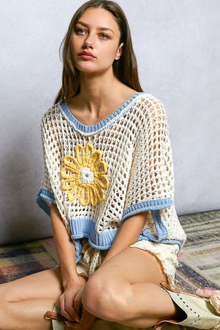 Woman wearing a crochet top with a yellow flower design on a neutral background