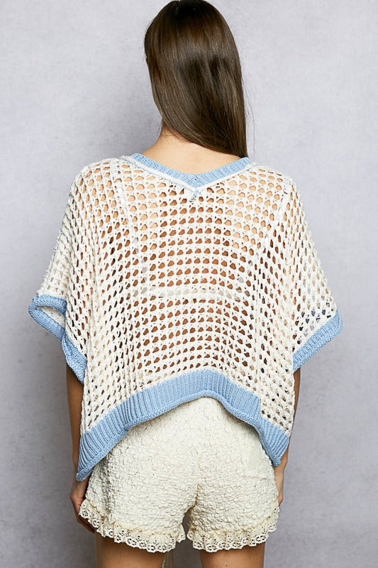 Woman wearing a crochet poncho with blue trim on a plain background